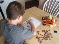 22-the_same_worksheet,but_with_real_coins_using_the_money_in_his_piggy_(airplane)_bank