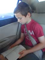 01-reading_his_book_in_the_car_while_driving_to_meet_a_friend_to_practice_baseball